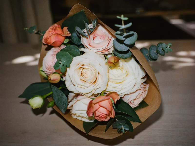Bouquet rond de roses de jardin, renoncules et eucalyptus en papier kraft sur un comptoir en bois