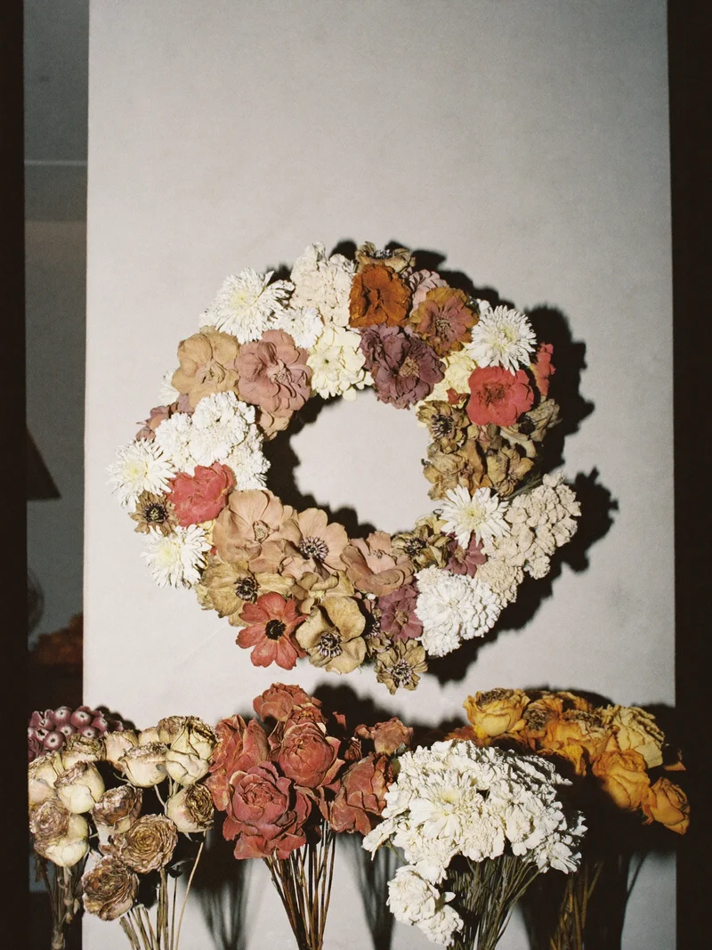 Couronne de fleurs séchées et bouquets d'immortelles aux tons naturels accrochés à un mur rustique