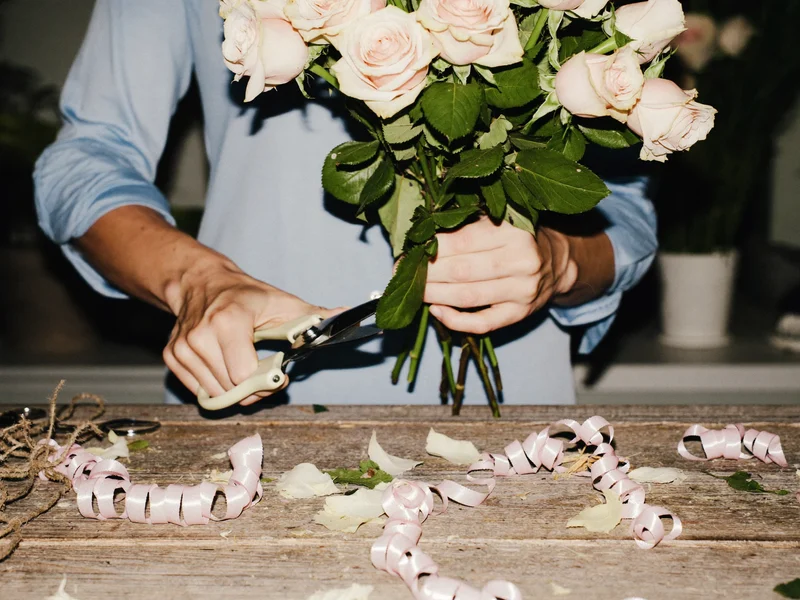Mains de fleuriste coupant des tiges de roses au sécateur sur un établi garni de ruban